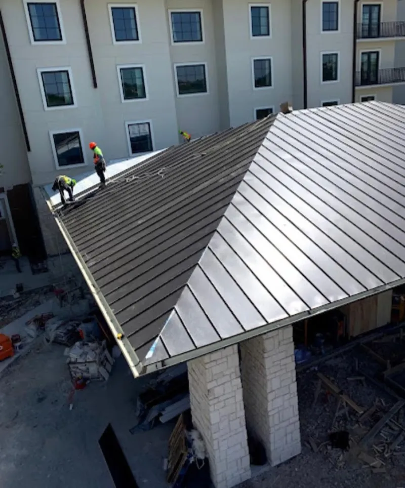 Crew installing standing seam metal roof panels on a commercial project in East Allen